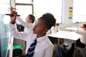 female high school students wearing uniform using interactive whiteboard during lesson