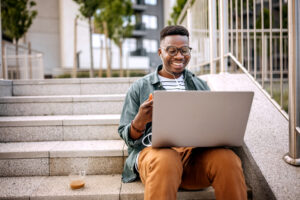 HIGHER EDUCATION PRODUCTS smiling student sitting on stairs using laptop
