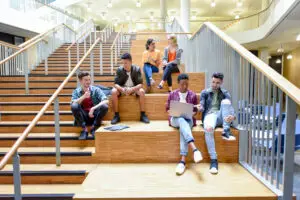 HIGHER EDUCATION PRODUCTS college friends sitting on steps in modern interior, chatting and using laptop